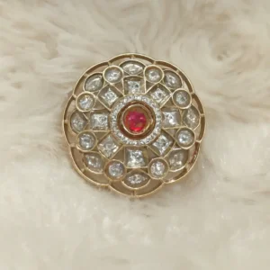 “Elegant gold-plated circular pendant with a ruby-red center stone surrounded by polki-style CZ diamonds, displayed on a soft ivory background.”