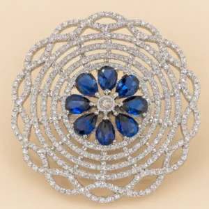 Close-up image of a Royal Sapphire-Blue Floral CZ Lattice Statement Ring by Risha Fine Jewels, featuring a sapphire-blue teardrop CZ floral cluster surrounded by an intricate multi-layered diamond-cut CZ lattice design, held against a natural green leaf background.