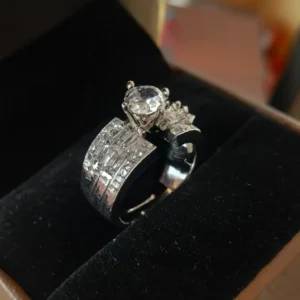 High-resolution image of a sparkling silver statement ring featuring a round solitaire center stone with baguette-cut CZ accents, displayed in a black velvet jewellery box – Risha Fine Jewels.
