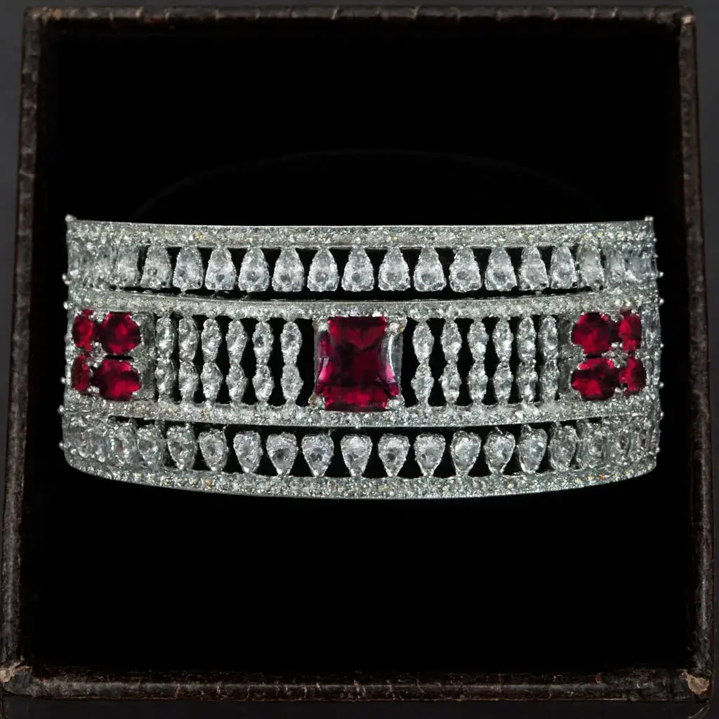 White-Gold Plated CZ Bracelet with Ruby Accents White-gold plated CZ statement bracelet with ruby accents for women by Risha Fine Jewels, featuring wide designer band with sparkling cubic zirconia stones and ruby crystals.